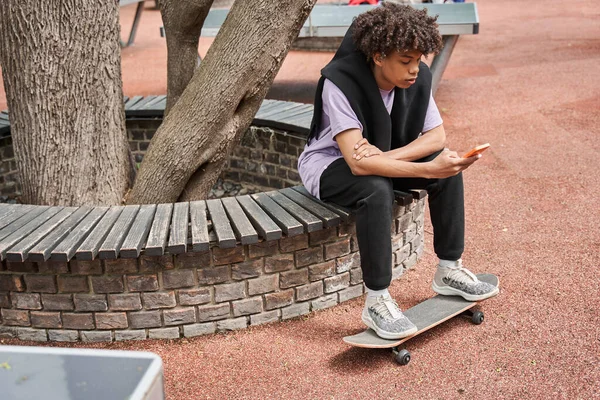 Man zit aan de bank en houdt zijn benen vast aan het skateboard terwijl hij surft op internet — Stockfoto