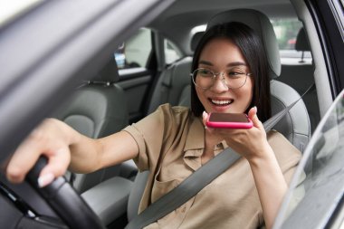 Kadın araba kullanırken cep telefonuyla konuşuyor.