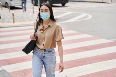 Şehirde yürürken yolda yürürken koruyucu maske takan bir kadın.