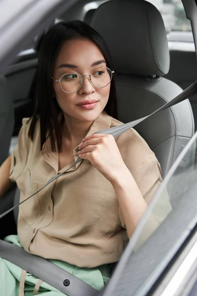 Mujer poniéndose el cinturón de seguridad mientras está sentada en el coche y mirando hacia la ventana — Foto de Stock