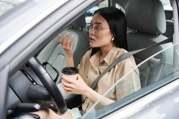 Woman drinking coffee and telling something emotionally while driving a car