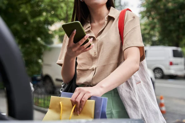 買い物袋をはきながらスマホを持って誰かにメッセージを書く女 — ストック写真