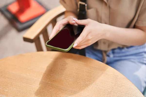 カフェのテーブルに座り、注文前にスマートフォンを持っている女性 — ストック写真