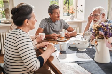 Huzurevinde yaşlılar masanın başında oturup sohbet ediyorlar.