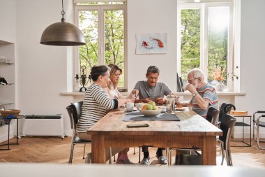 Emekliler bakıcılarıyla masada oturuyor ve kartlarla oynuyorlar.