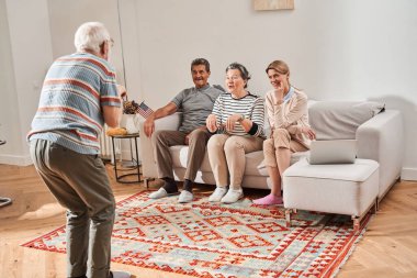 Emeklilerin ve bakıcıların önünde duran ve bir şeyler gösteren kıdemli adam.