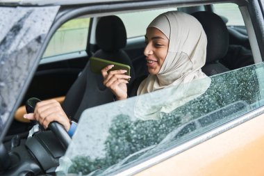 Bir kadın araba kullanırken akıllı telefonuyla arkadaşına bir şey söylüyor.