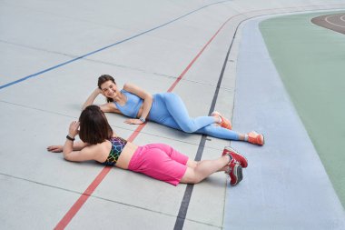 Spor kıyafetli bir kadın antrenmandan sonra dinleniyor ya da bir stadyum pistinde uzanırken koşuyor.
