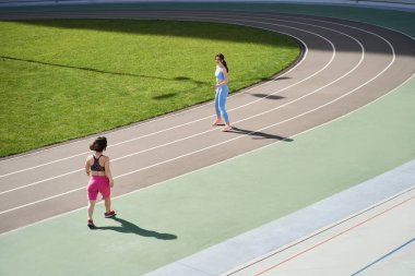 Kadın stadyumda yürüyor ve cüce arkadaşına gülümsüyor.