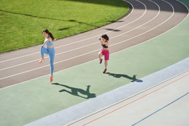 Stadyumda çeşitli kızlar antrenman yapıyor ve koşuyor.