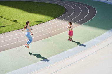 Güneşli bir sabahta stadyumda ip atlayan en iyi arkadaşına bakan kadın.