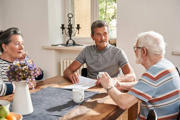 Oudere mensen zitten aan tafel voor elkaar en drinken thee — Stockfoto