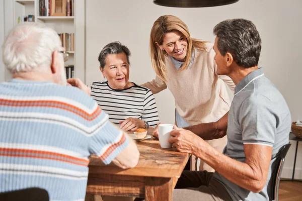 Oudere mensen zitten aan tafel en praten met vriendelijke verpleegster in het bejaardentehuis — Stockfoto