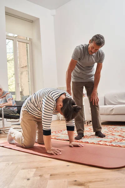 Senior man looking how his female friend doing morning exercises — Stock Photo, Image