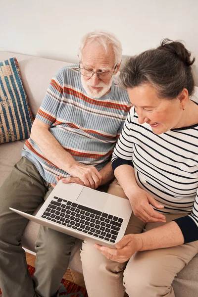 Couple d'âge mûr tenant un ordinateur portable et regardant l'écran et discuter de quelque chose — Photo