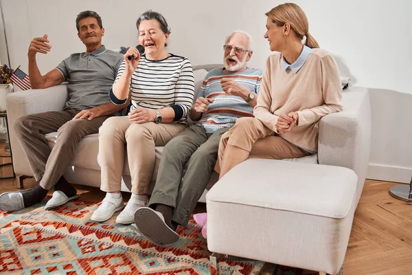 Groep senioren die zingen terwijl ze met hun verzorger op de bank zitten — Stockfoto