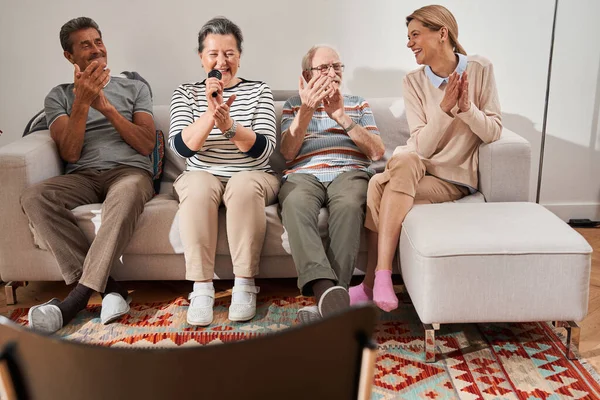 Groep senioren die zingen terwijl ze met hun verzorger op de bank zitten — Stockfoto