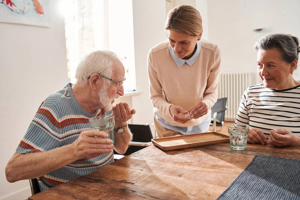 Vriendelijke zorgverlener die medicijnen geeft aan oudere mannen en vrouwen — Stockfoto