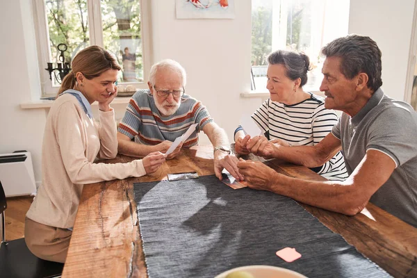 Verzorger zit aan tafel met gepensioneerden en kijkt naar foto 's — Stockfoto