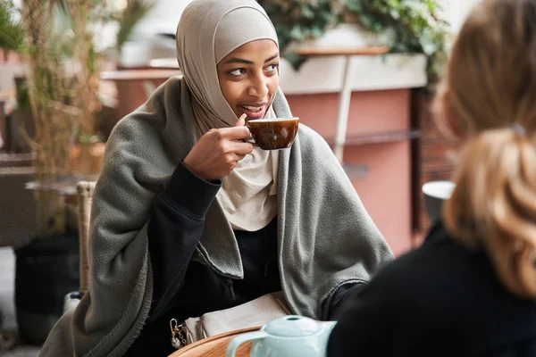 Woman sitting at the table outdoors and chatting with her female friend