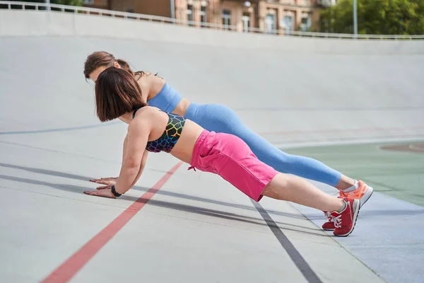 Cüce en iyi arkadaşıyla stadyumda planking egzersizi yapan bir kadın. — Stok fotoğraf