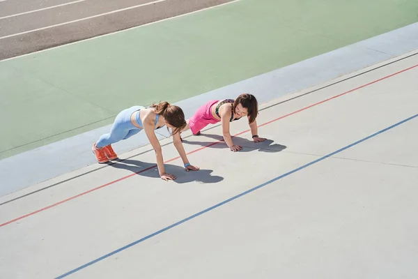 Женщина делает упражнения на доске на стадионе в компании своего лучшего друга-карлика — стоковое фото