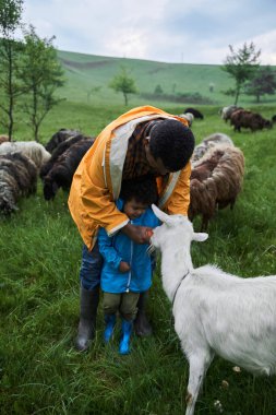 Havuç tutan ve babasıyla vakit geçirirken keçiye veren çocuk.