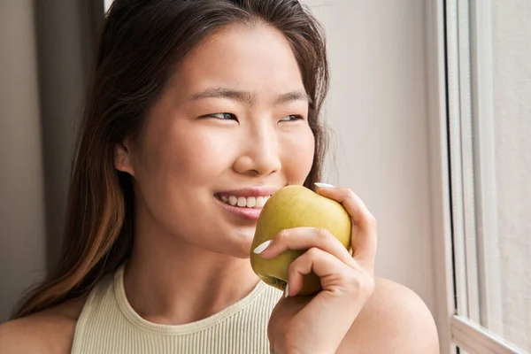 Mujer mirando a la ventana y comiendo manzana mientras pasa la mañana —  Fotos de Stock