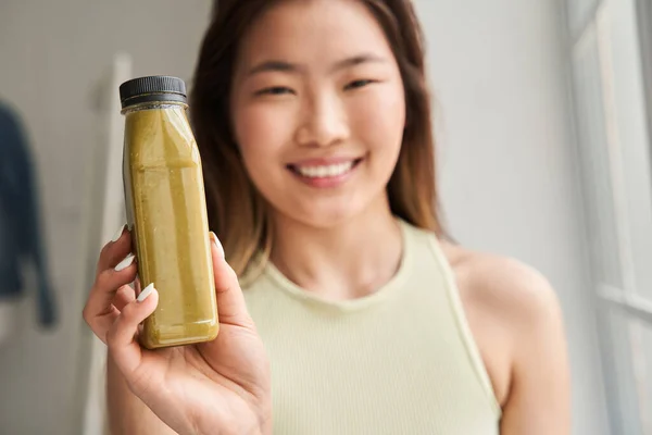 Laughing young woman showing to the camera fruit or vegetable smoothie — Stock Photo, Image