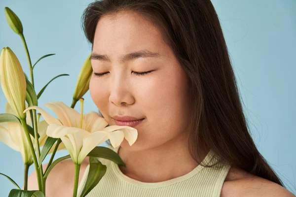 Aziatische vrouw ruikt bloemen met gesloten ogen terwijl poseren in de studio — Stockfoto