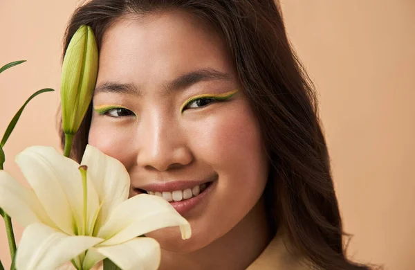 Mujer con maquillaje creativo posando con rama de lirio cerca de su cara —  Fotos de Stock