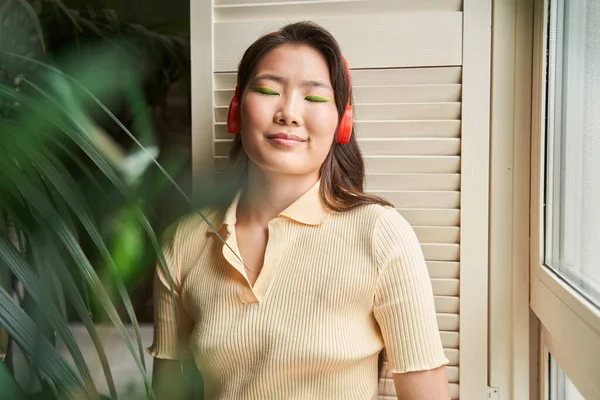 Señora con auriculares apoyados en la pared con los ojos cerrados y escuchando música —  Fotos de Stock