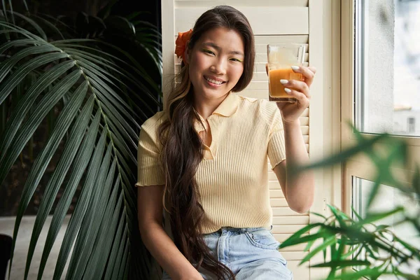 Chica sosteniendo un vaso de jugo de naranja o zanahoria y sonriendo a la cámara —  Fotos de Stock