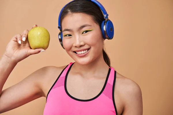 戴耳机的女人，一边听着她最喜欢的音乐，一边拿着苹果 — 图库照片