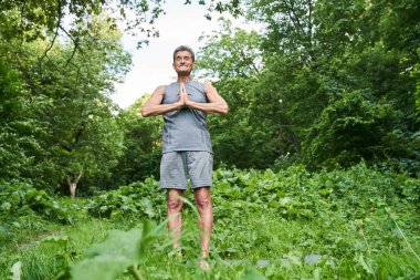 Parkta dua jesti yaparak boş bir pozisyonda oturan bir adam gözlerini kapalı tutuyor.