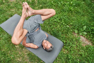 Yoga minderinde uzanan ve jimnastik yapan bir adam elleriyle vücudunu tutuyor.