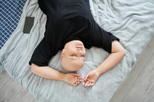 Vrouw in koptelefoon liggend aan het bed en luisterend naar muziek terwijl ze het weekend thuis doorbrengt — Stockfoto