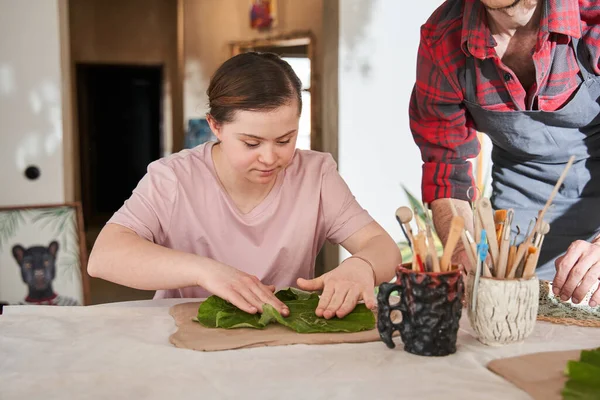 Girl with down syndrome impressing green leaf to the clay — Stock Photo, Image