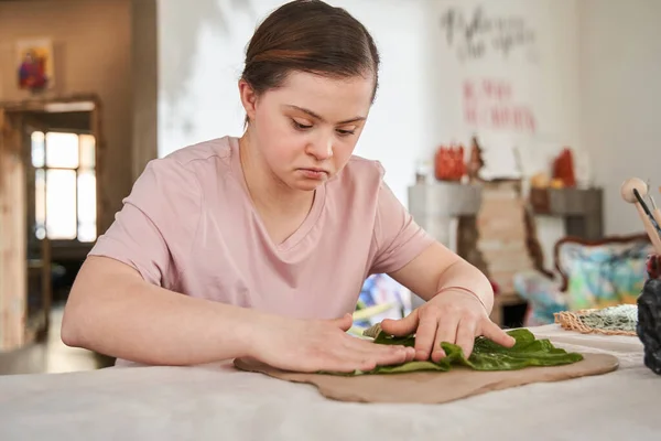 Girl with down syndrome impressing green leaf to the clay — Stock Photo, Image