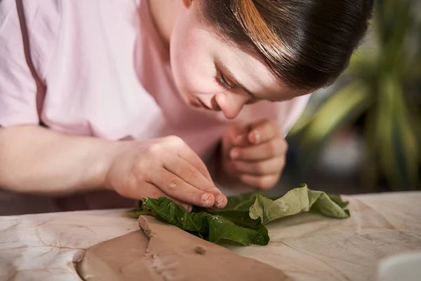 Mujer tocando con el dedo la hoja fresca mientras imprime textura de la misma a la arcilla — Foto de Stock