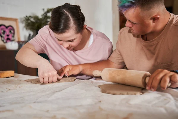 Garçon avec des besoins spéciaux déroulant l'argile tout en regardant comment son ami sculpter — Photo