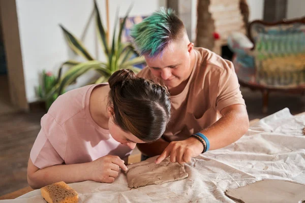 Chłopiec z kolorowymi włosami pomaga swojej dziewczynie rzeźbić z gliny podczas zajęć mistrzowskich — Zdjęcie stockowe