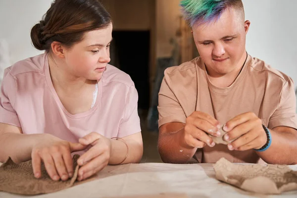 Tieners met down syndroom kijken elkaar aan terwijl ze gerechten maken van klei — Stockfoto