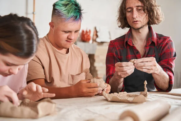 Rzemieślnik uczy młodych ludzi ze specjalnymi potrzebami przygotowywania talerzy z gliny — Zdjęcie stockowe