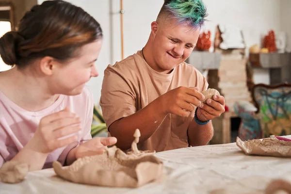 Ragazza con la sindrome di Down guardando il suo ragazzo con i capelli colorati mentre teneva argilla — Foto Stock