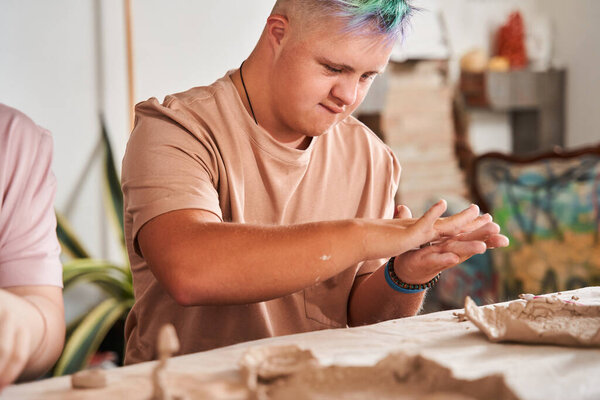 Мальчик с синдромом Дауна с цветными волосами держит кусок глины и готовит новое блюдо
