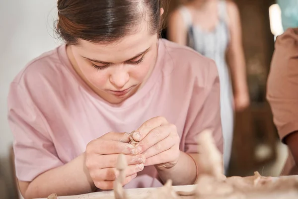 Kobieta ze specjalnymi potrzebami badająca glinę podczas pracy przy stole podczas warsztatów rzeźbiarskich — Zdjęcie stockowe