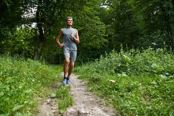 Hombre corriendo en el parque de verano por la mañana mientras entrena y escucha los sonidos de la naturaleza — Foto de Stock