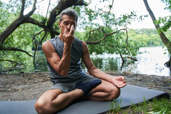 Мужчина делает дыхательные упражнения, закрывая одну ноздрю пальцем во время сидения — стоковое фото