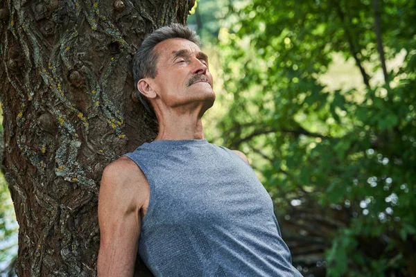 El hombre mantiene los ojos cerrados y relajándose en el bosque mientras está acostado en el tronco — Foto de Stock